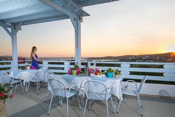 Terrasse des Pyrgaki Hotels mit Blick auf den Sonnenuntergang und mehreren gedeckten Tischen.