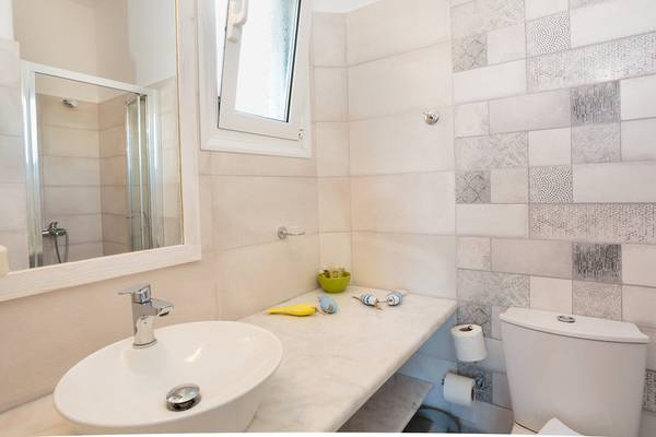 Badezimmer im Pyrgaki Hotel mit weißem Waschbecken, Spiegel, Duschkabine und gefliester Wand.
