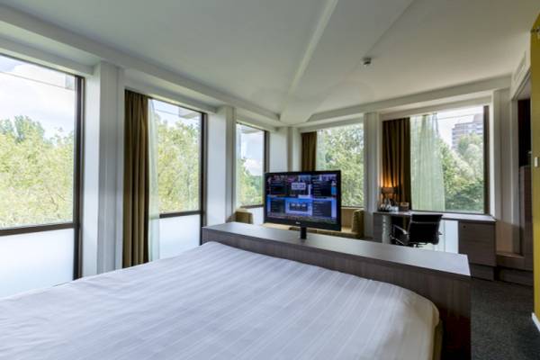 Leonardo Hotel Amsterdam Rembrandtpark Hotelzimmer mit Fernseher, Schreibtisch und Fenstern.