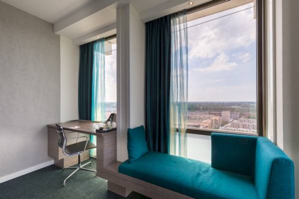 Innenansicht eines Zimmers im Leonardo Hotel Amsterdam mit Schreibtisch, Stuhl und Fenstern.