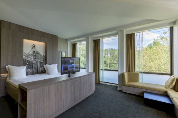 Innenansicht eines Schlafzimmers im Leonardo Hotel Amsterdam Rembrandtpark mit Doppelbett, Fernseher und Fenstern.