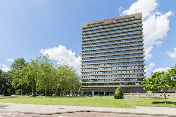Leonardo Hotel Amsterdam Rembrandtpark Gebäude mit vielen Fenstern und Bäumen davor.