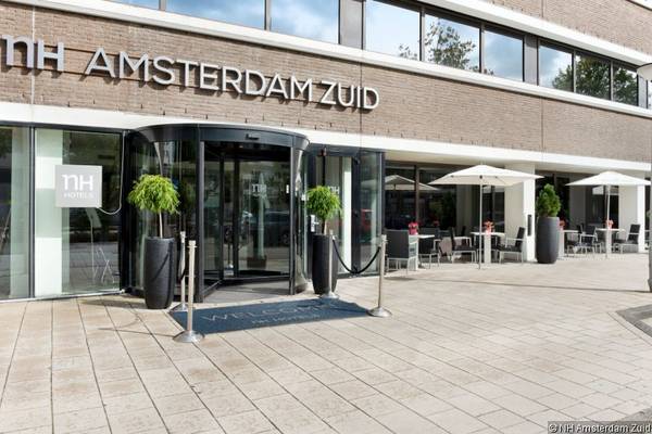 Vorderansicht des NH Amsterdam Zuid Hotels mit Eingang und Sitzbereichen draußen