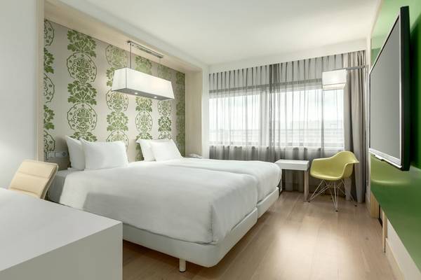 Doppelbett-Zimmer im NH Amsterdam Zuid Hotel mit grünen und weißen Wandmustern, zwei Betten, Schreibtisch und Fernseher.