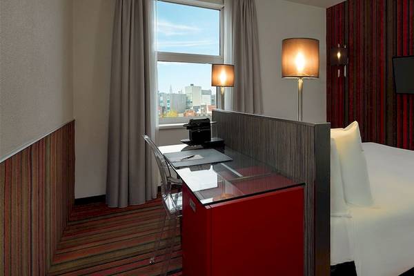Ein modernes Hotelzimmer mit einem Bett, einem Schreibtisch, einem Fenster und zwei Lampen.