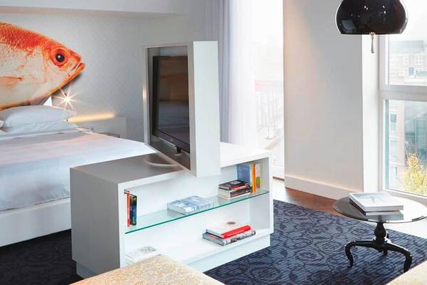 Schlafzimmer im Andaz Amsterdam Hotel mit Fischwand, Bett, Fernseher, Bücherregal und Fenster.