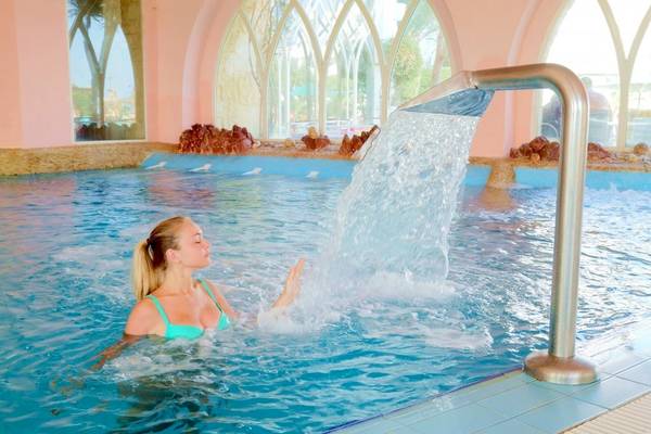 Frau genießt Wasserfall im Schwimmbad des Lella Baya & Thalasso Hotels
