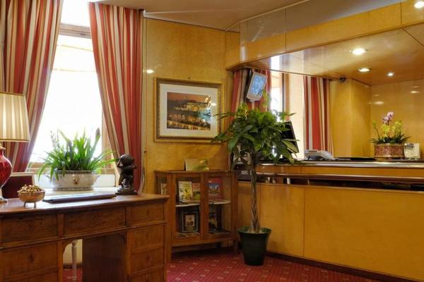 Rezeption des Atlante Star Hotels mit Schreibtisch, Pflanzen und gerahmtem Bild.
