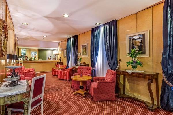 Innenansicht des Atlante Star Hotels mit rotem Teppichboden, roten Sesseln, Tischen und einem gerahmten Bild an der Wand.