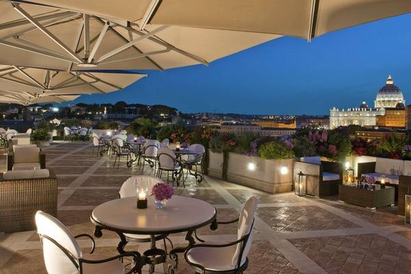 Abendliche Hotelterrasse mit Tischen, Stühlen und Schirmen, Blick auf Rom