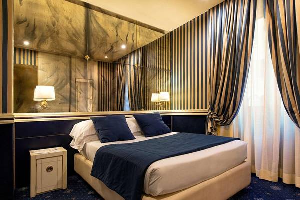 Bett im Hotelzimmer des Atlante Star mit blauer Bettwäsche und Dekor.