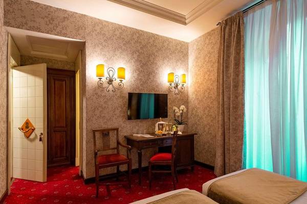 Zimmer im Atlante Star Hotel mit zwei Betten, Fernseher, Schreibtisch und Stühlen.