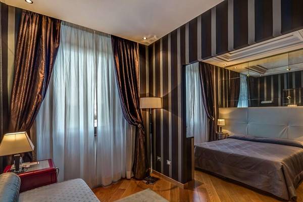 Schlafzimmer im Atlante Star Hotel mit Doppelbett, Nachttischen und Wandleuchten.
