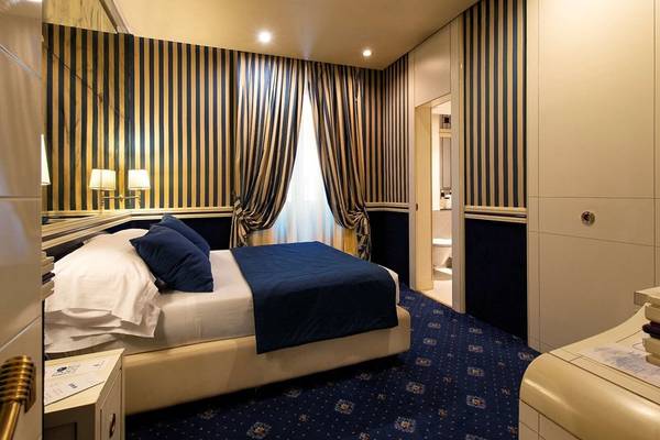 Schlafzimmer im Atlante Star Hotel mit blauen und gelben gestreiften Wänden, Doppelbett, Nachttisch und offenem Badezimmer.