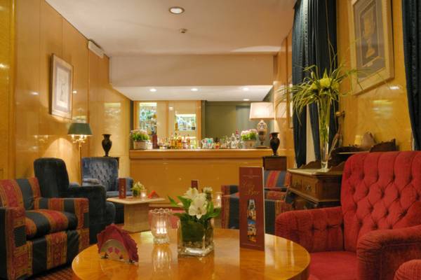 Lobby-Lounge des Atlante Star Hotels mit Sitzmöbeln, einem runden Tisch und einem Tresen.
