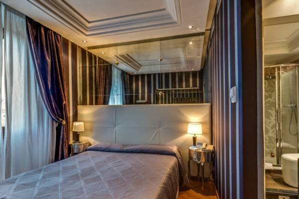 Schlafzimmer im Atlante Star Hotel mit einem Bett, zwei Lampen und einem großen Spiegel.