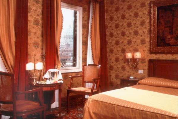 Ein Schlafzimmer im Atlante Star Hotel mit floralem Tapetendesign, einem Bett, zwei Sesseln und einem kleinen Tisch.