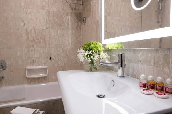 Badezimmer im Bettoja Hotel Massimo d'Azeglio mit Waschbecken, Spiegel und Badewanne.