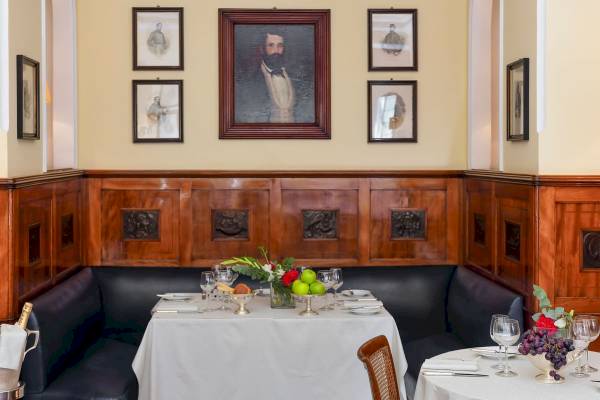 Innenansicht des Speisebereichs im Bettoja Hotel Massimo d'Azeglio mit gedeckten Tischen, Blumen und Porträts an der Wand.