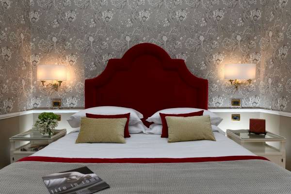 Schlafzimmer im Bettoja Hotel Massimo d'Azeglio mit rotem Kopfteil und floralem Wandmuster.
