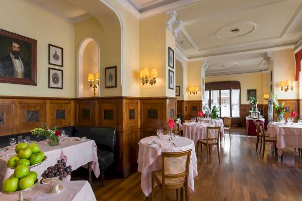 Innenansicht des Restaurants im Bettoja Hotel Massimo d'Azeglio mit gedeckten Tischen, Holzböden und Wandgemälden.