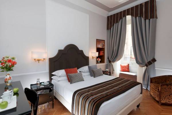 Ein elegantes Hotelzimmer im Bettoja Hotel Massimo d'Azeglio mit einem Bett, Tisch, Blumen und Fenstern.