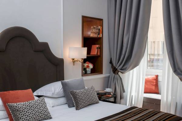 Zimmer im Bettoja Hotel Massimo d'Azeglio mit Bett, Kissen, Lampe und Bücherregal.