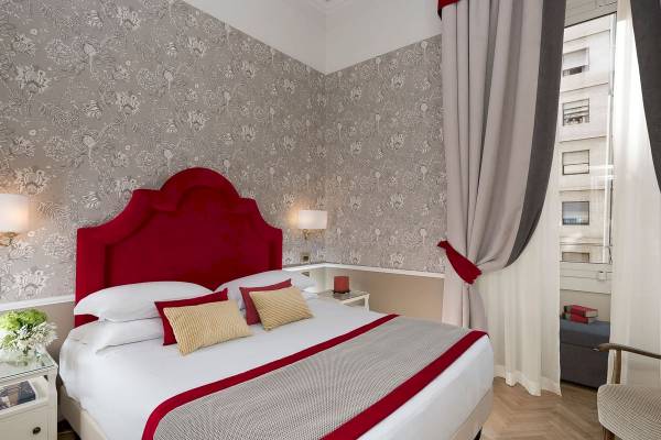Schlafzimmer im Bettoja Hotel Massimo d'Azeglio mit floralem Wandmuster und rotem Kopfteil.