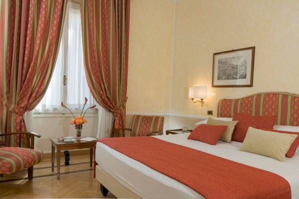 Schlafzimmer im Bettoja Hotel Massimo d'Azeglio mit Bett, Kissen, Nachttisch und Fenstern.