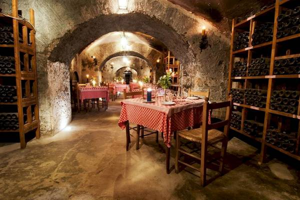 Restaurantkeller im Bettoja Hotel Massimo d'Azeglio mit roten Tischdecken und Weinflaschen in Regalen.