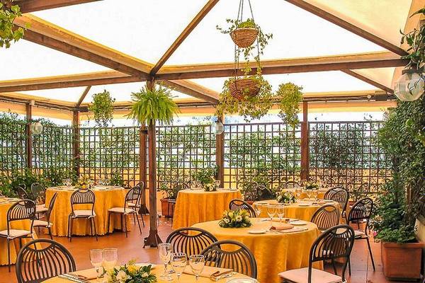 Garten-Terrasse des Pineta Palace Hotels mit runden Tischen, Stühlen und gelben Tischdecken, umgeben von Pflanzen und Blumen.