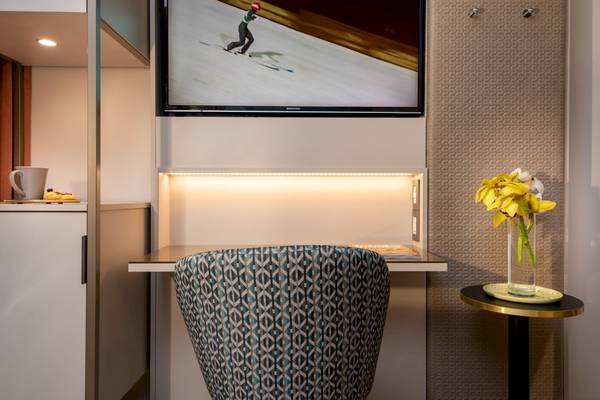 Hotelzimmer mit Schreibtisch, Fernseher und Blumenvase auf einem Beistelltisch.