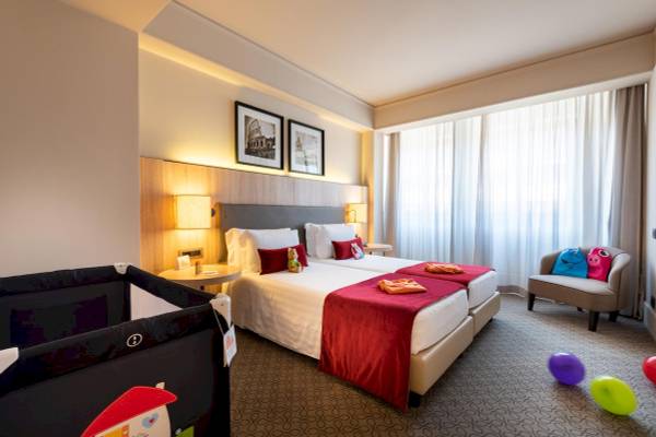 Innenansicht eines Zimmers im A.Roma Lifestyle Hotel mit zwei Betten, Dekor und Spielzeug.
