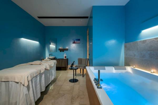 Spa-Behandlungsraum im A.Roma Lifestyle Hotel mit blauen Wänden, Liegen und Badewanne.