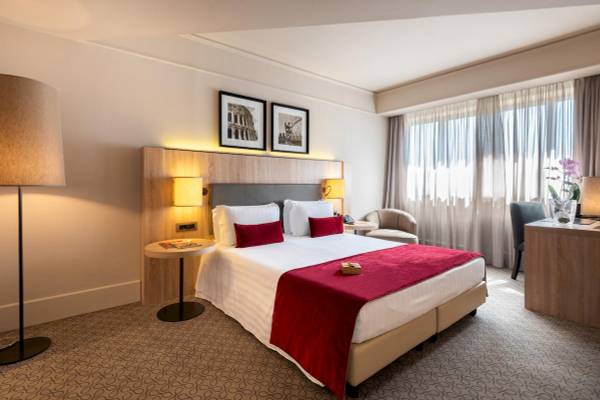 Innenansicht eines Zimmers im A.Roma Lifestyle Hotel mit Doppelbett, Schreibtisch, Sesseln und Lampen.