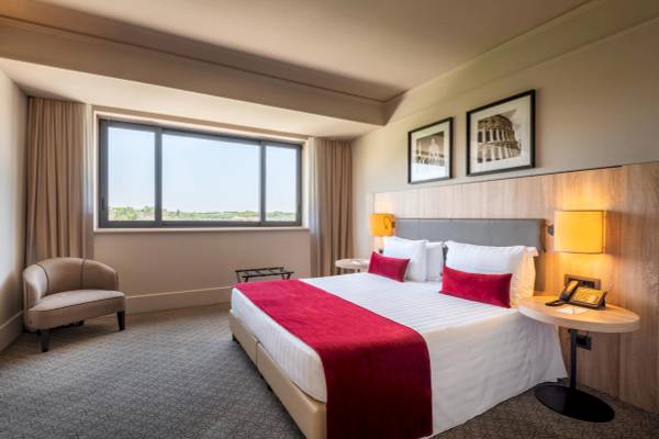 Innenansicht eines Zimmers im A.Roma Lifestyle Hotel mit Bett, Sessel und Schreibtisch.