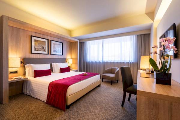 Innenansicht eines Schlafzimmers im A.Roma Lifestyle Hotel mit Bett, Nachttischen, Lampen, Stühlen und einem Schreibtisch.