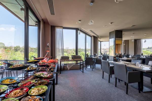 Innenansicht des Restaurants im A.Roma Lifestyle Hotel mit großen Fenstern und Blick auf die Landschaft.