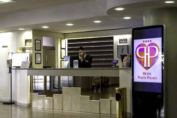 Hotelrezeption mit digitalem Schild und Mitarbeiter, der telefoniert.
