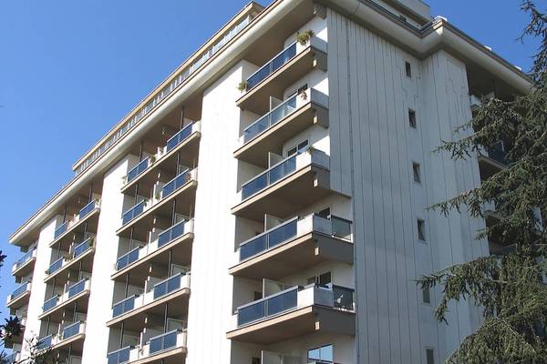 Ein weißes Hochhaus mit mehreren Balkonen und einem großen Baum davor.
