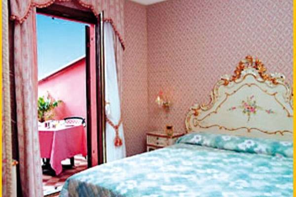 Schlafzimmer im Tre Archi Hotel mit rosa Wänden, offenem Balkon und Tisch mit roter Tischdecke.