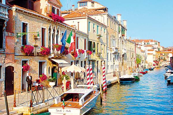 Ein Kanal in Venedig mit bunten Gebäuden, Booten und blühenden Pflanzen.