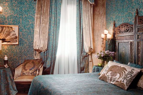 Schlafzimmer im Metropole Hotel mit blauen Wandverzierungen, Vorhängen und einem Bett mit dekorativen Kissen.