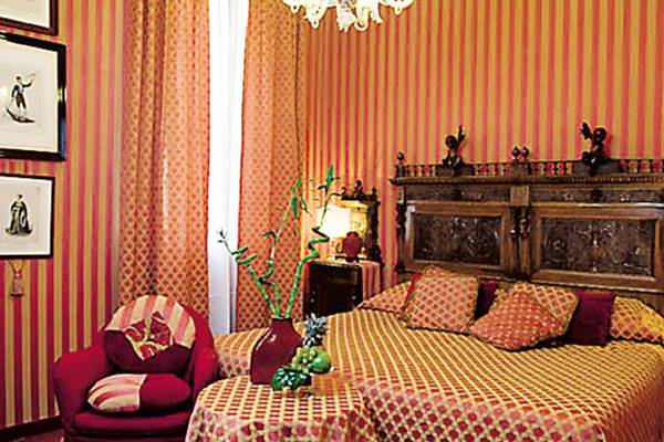 Schlafzimmer im Metropole Hotel mit zwei Betten, rotem Sessel, und kunstvollen Wandverkleidungen.