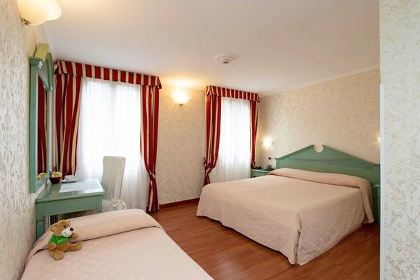 Zweibettzimmer im Tintoretto Hotel mit grünen Kopfteilen, weißen Laken und roten Vorhängen.