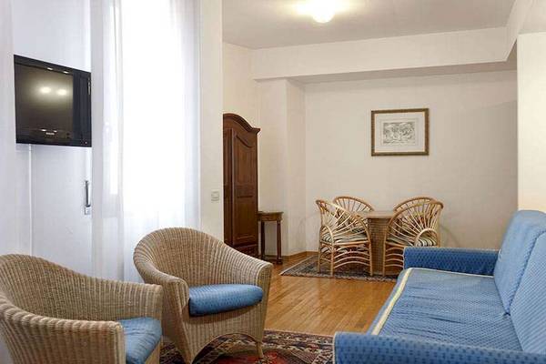 Wohnzimmer im San Marco Palace Hotel mit Fernseher, Korbstühlen und Tisch.