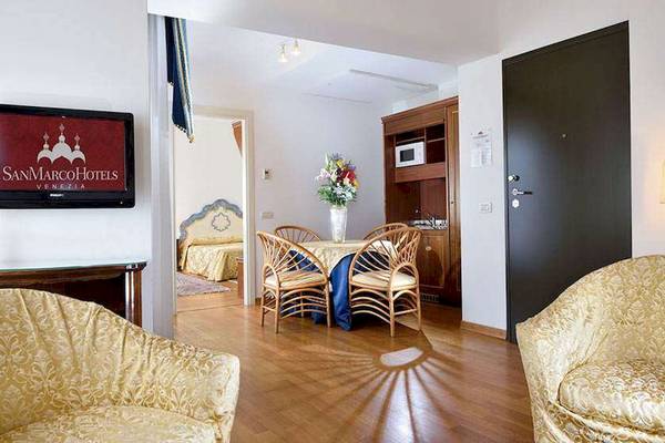 Innenraum des San Marco Palace Hotels mit Wohnzimmer, Esstisch, Fernseher und Schlafzimmer.