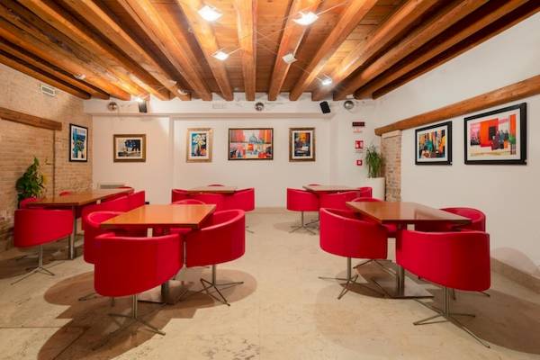 Innenbereich des Eurostars Residenza Cannaregio mit Holzdecken, roten Stühlen und Tischen sowie Gemälden an der Wand.