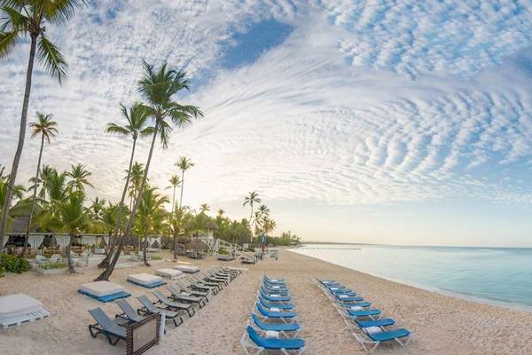 Sonnenuntergang am Strand des Catalonia Bayahibe Hotels mit blauen Liegestühlen und Palmen