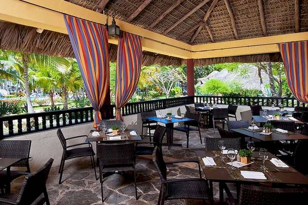 Terrasse des Restaurants im Catalonia Bayahibe Hotel mit bunten Vorhängen und Blick auf einen Pool.